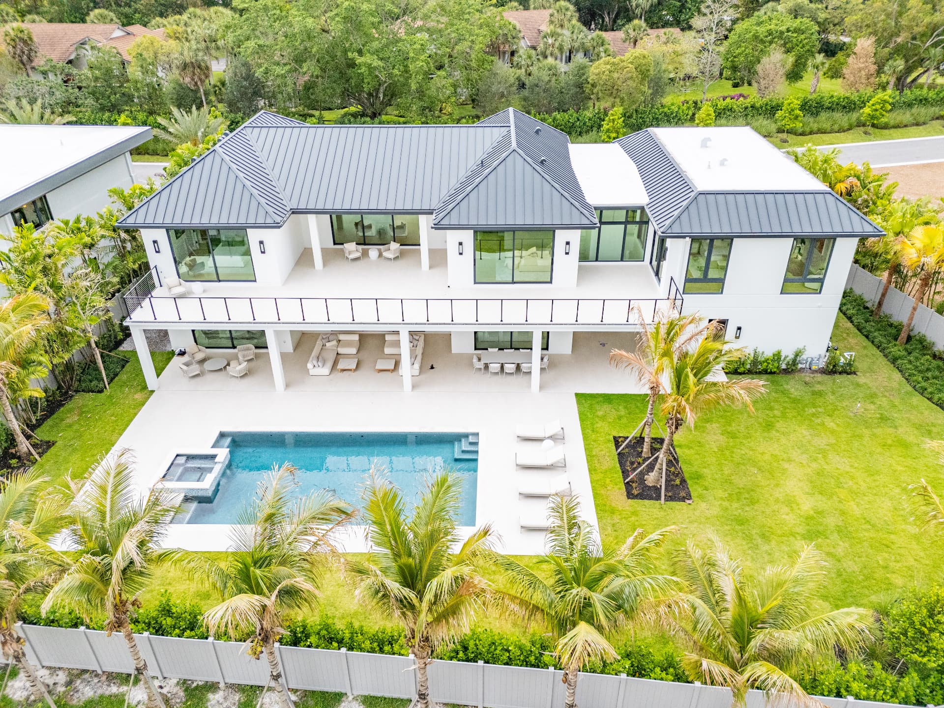 Rear elevation of a metal-roof custom residence with second-floor balcony and pool at Farrell Estates in Wellington, Florida