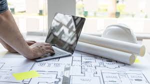 Architect using laptop with blueprints and helmet.