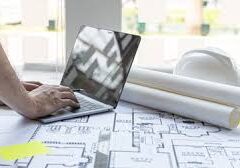 Architect using laptop with blueprints and helmet.